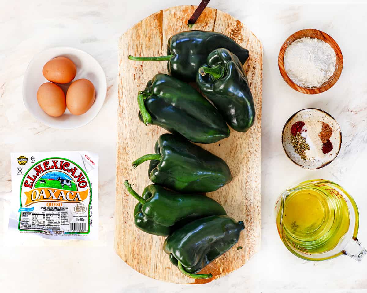 top view of chile relleno ingredients: poblano peppers, eggs, Oaxaca cheese, flour, vegetable oil, and spices