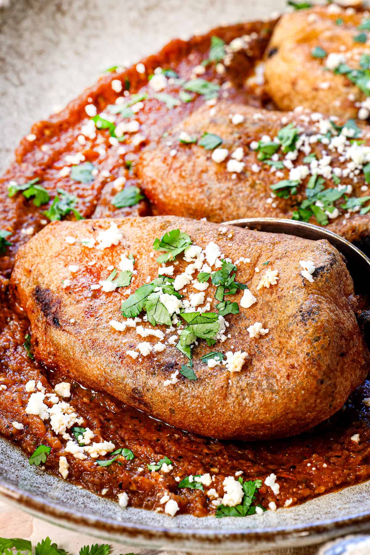 showing how to make chile rellenos by placing on top of salsa ranchera and garnishing with Cotija cheese and cilantro to serve