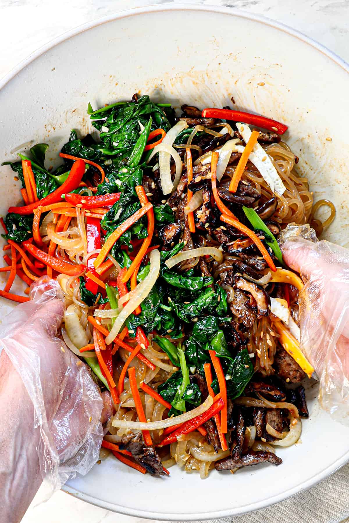 showing how to make Japchae by tossing the ingredients together with gloved hands