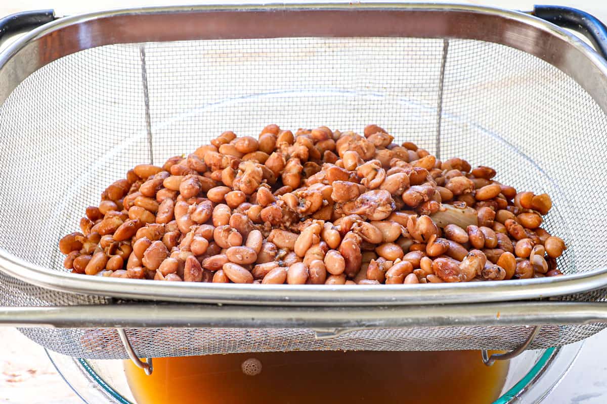 showing how to make refried beans by draining the cooked beans in a strainer over a bowl to catch the cooking liquid