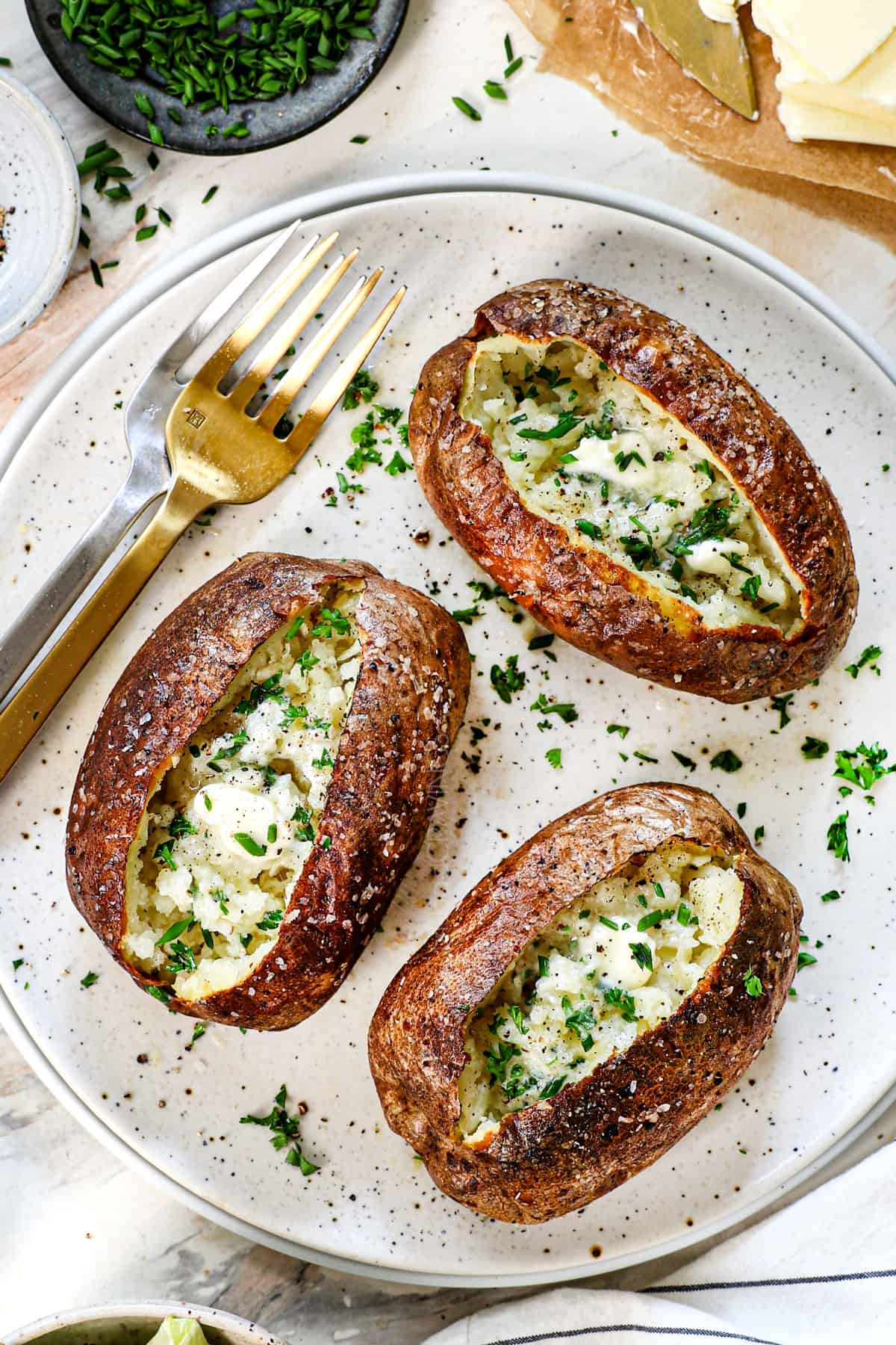 showing how to make baked potatoes in air fryer by transferring to a plate and topping with butter and chives