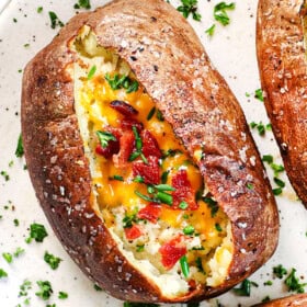 up close of baked potatoes in air fryer being served on a plate garnished with green onions