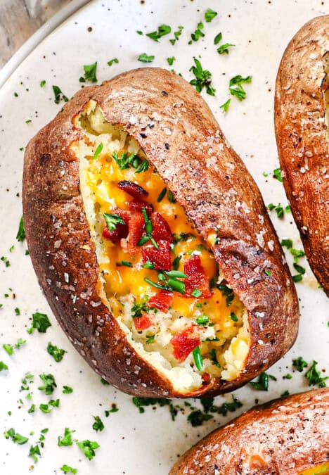 up close of baked potatoes in air fryer being served on a plate garnished with green onions