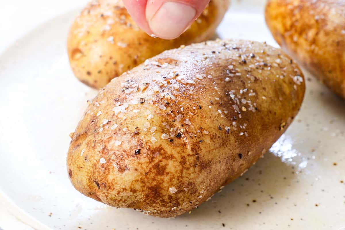showing how to make baked potatoes in air fryer by seasoning the potatoes with kosher salt and freshly cracked pepper