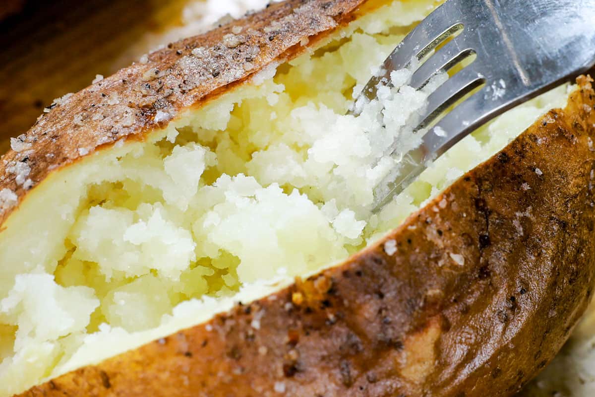 showing how to make baked potatoes in air fryer by fluffing the insides with a fork