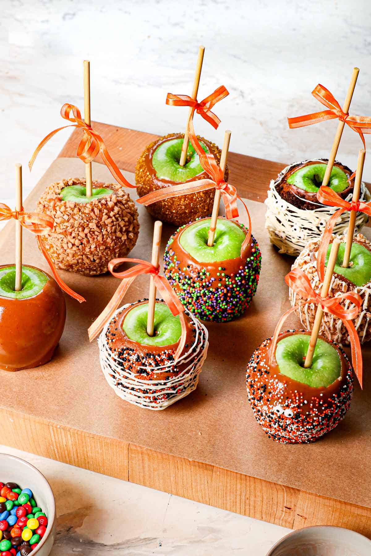 showing how to make caramel apples by lining on a cutting board and adding a ribbon bow after they are cooled.