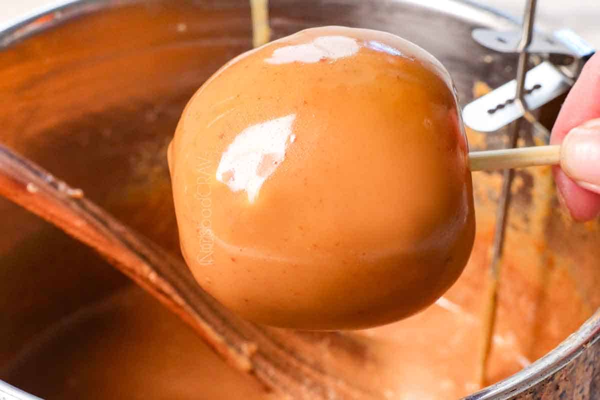 showing how to make caramel apples by dipping the apples in the caramel to coat