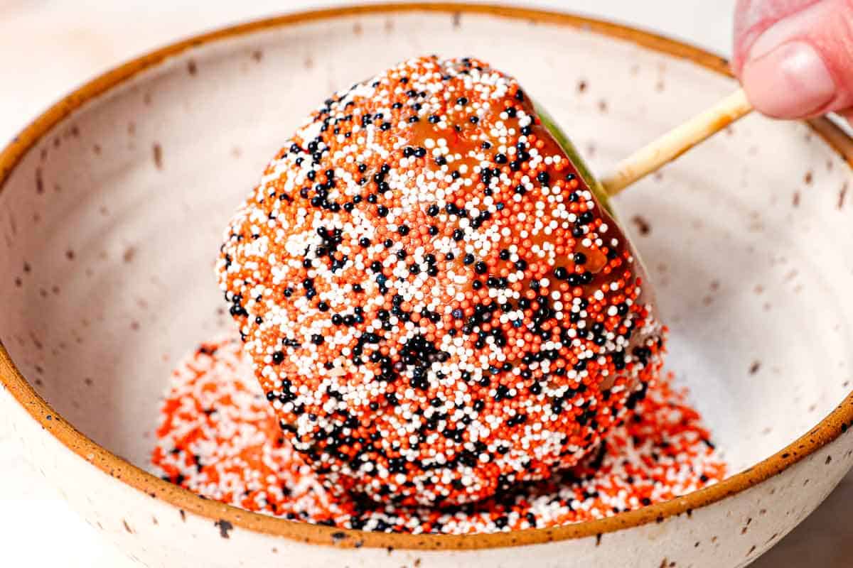 showing how to make caramel apples by decorating with sprinkles by rolling in a bowl of sprinkles