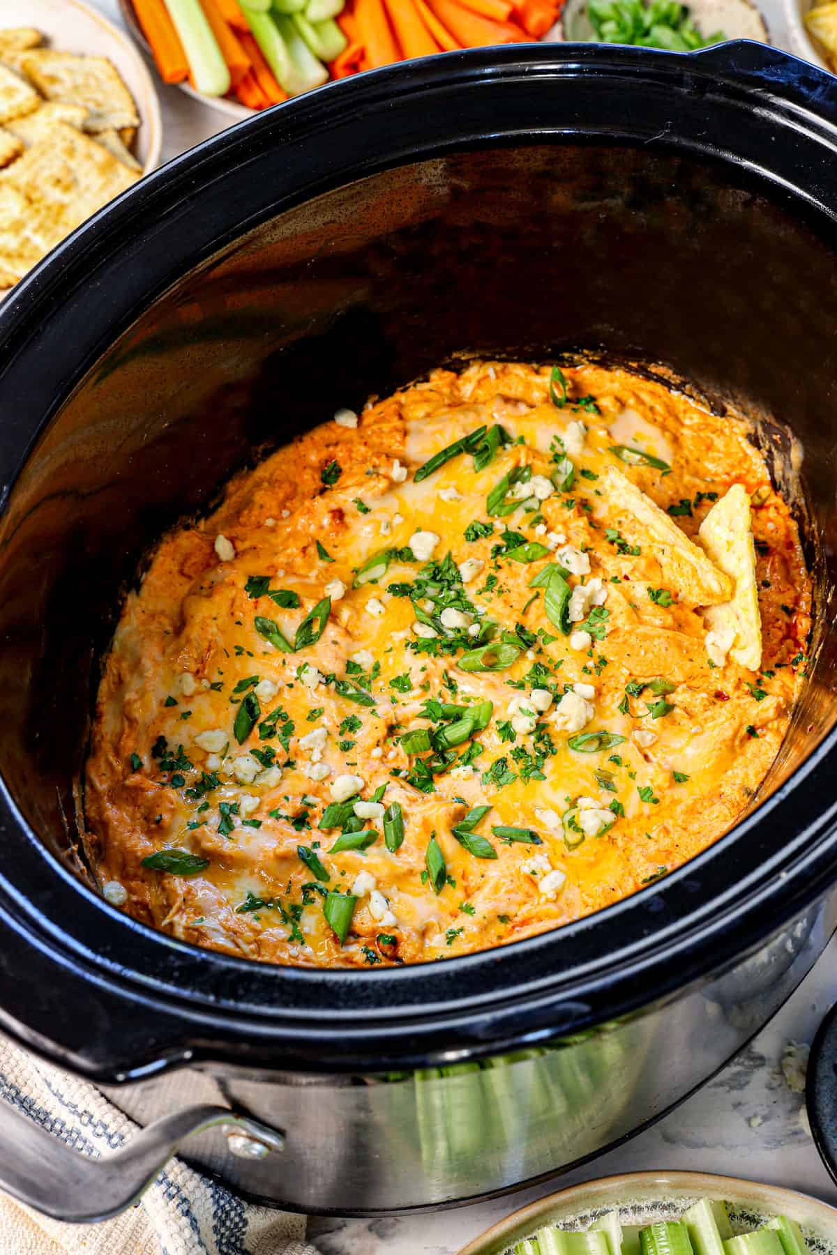 showing how to make crockpot buffalo chicken dip by garnishing with blue cheese crumbles and green onions