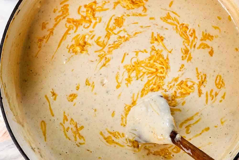 Showing how to make baked potato soup by stirring cheddar cheese into the soup