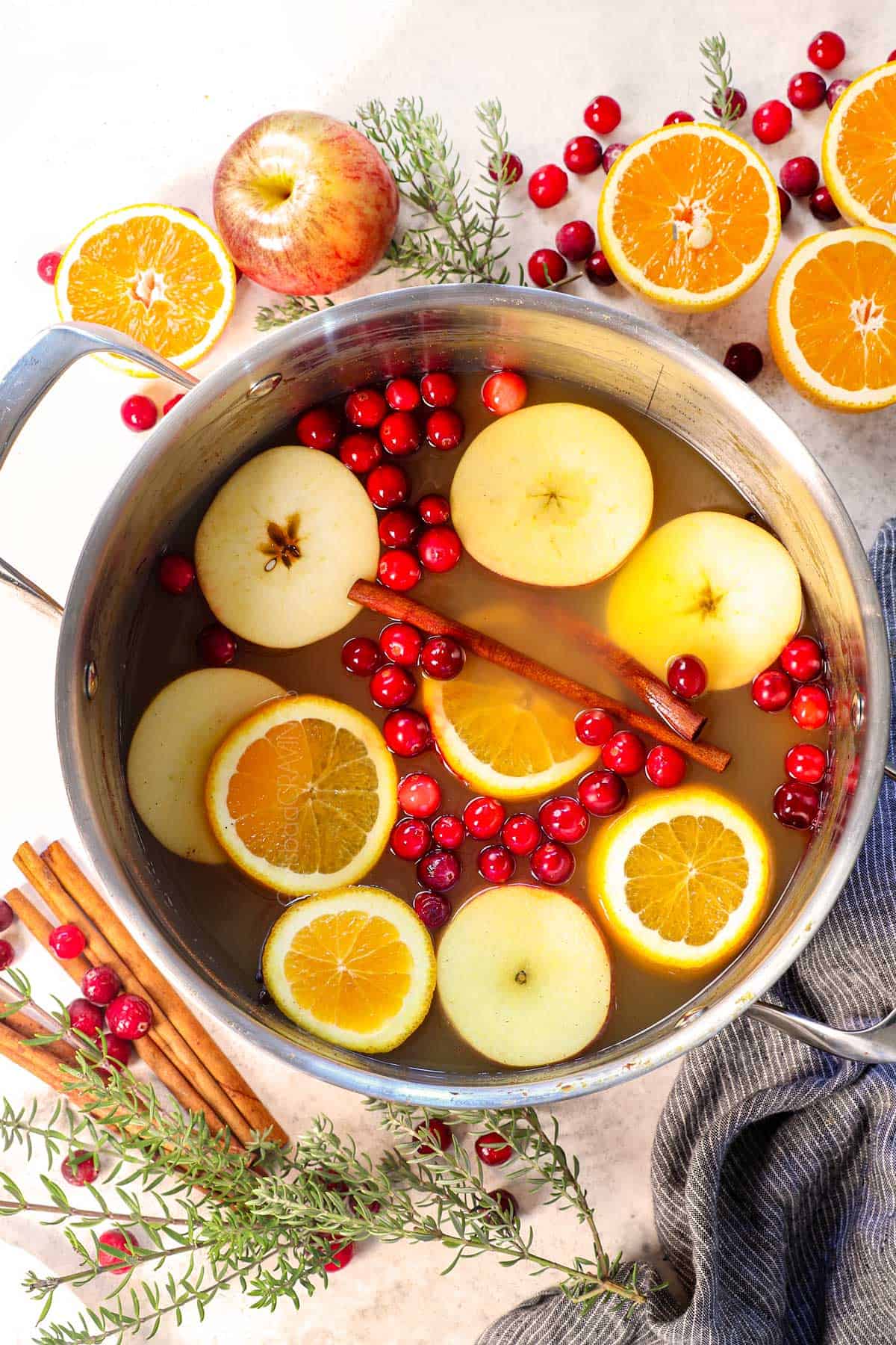 showing how to make wassail by garnishing with orange slices, apple slices, and cranberries
