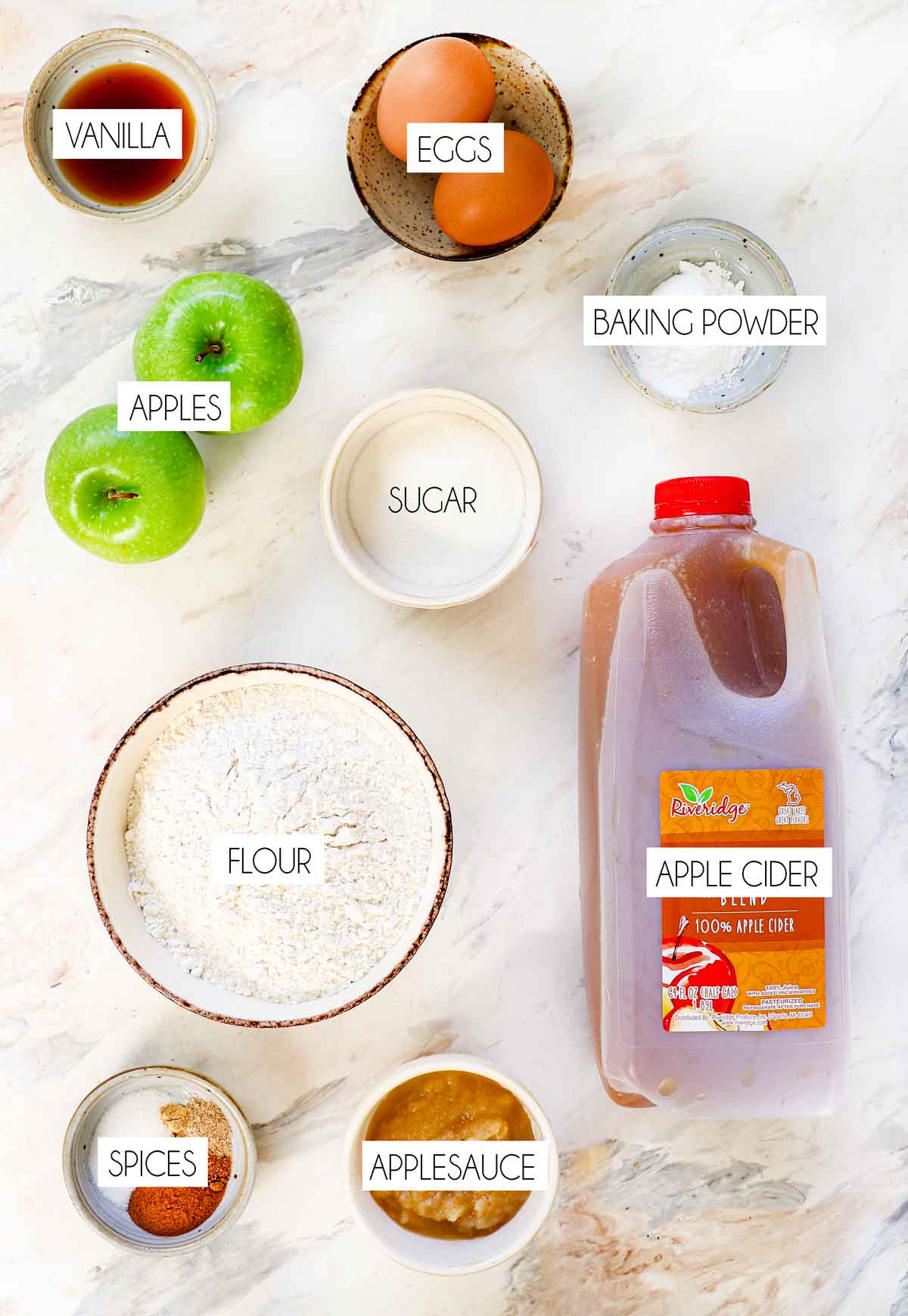 top view of apple fritter ingredients: flour, sugar, baking powder, eggs, apples, apple cider, applesauce, vanilla, ground cinnamon