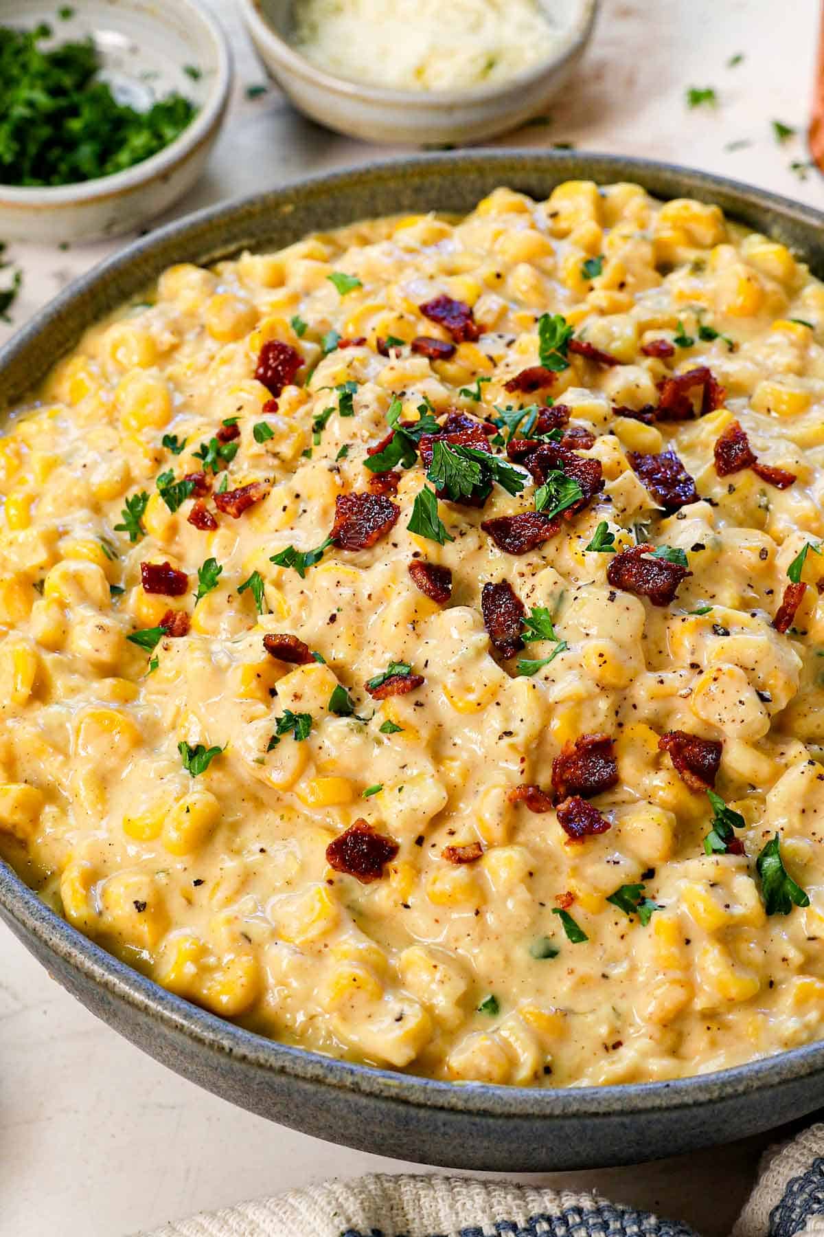 creamed corn recipe being served in a bowl garnished with bacon and parsley