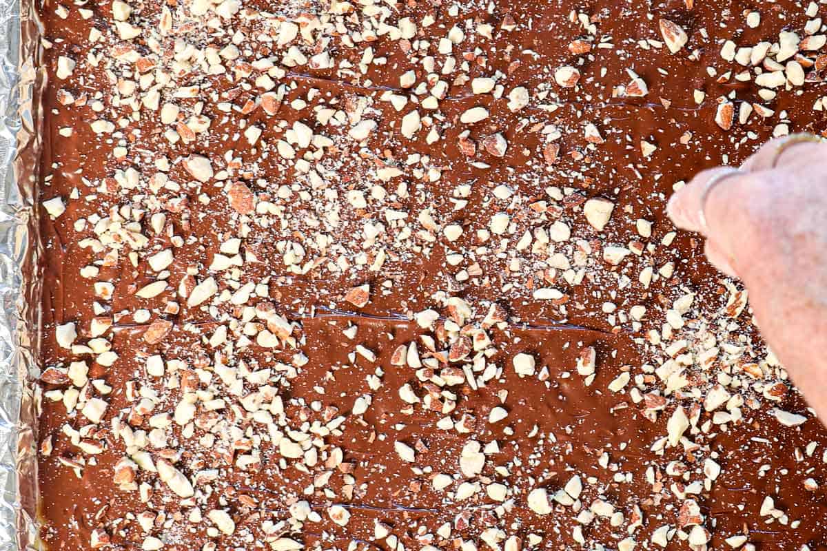 showing how to make almond roca by sprinkling the chopped almonds over the melted chocolate layer