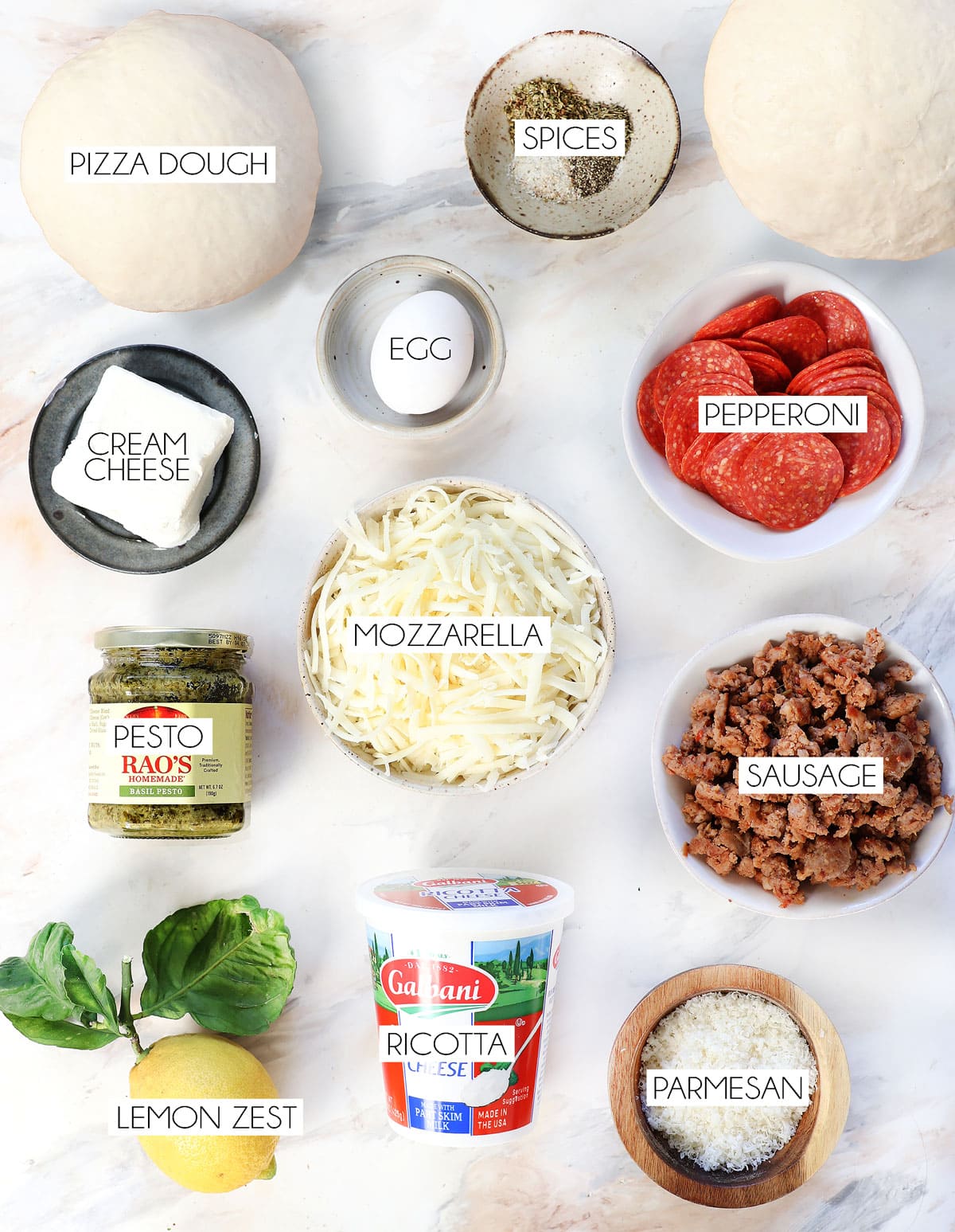 Top view of calzone ingredients: pizza dough, ricotta, sausage, pepperoni, mozzarella, Parmesan, oregano, basil