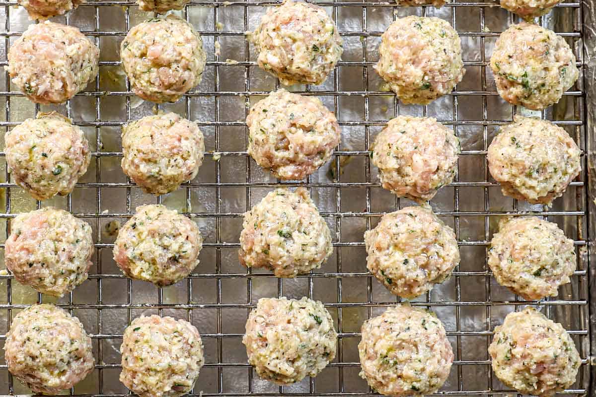showing how to make chicken meatballs by scooping the mixture by the 1 ยฝ tablespoon, then rolling into balls and placing on a baking rack
