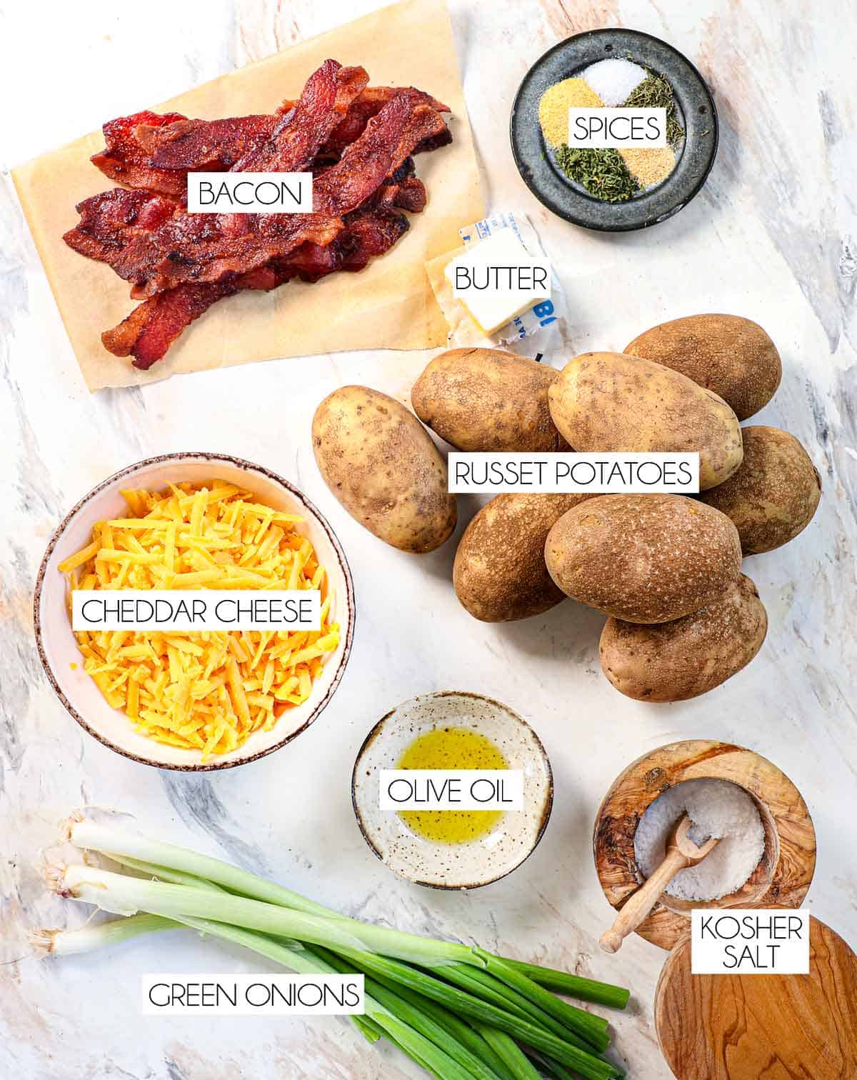 top view of potato skins recipe ingredients: Russet potatoes, cheddar cheese, butter, olive oil, spices, bacon, green onions, sour cream