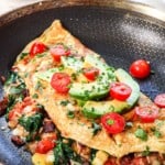 omelet in a skillet garnished with tomatoes, avocado and parsley, showing how to serve